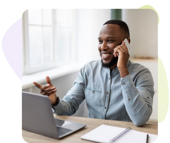Un homme assis à un bureau, parlant au téléphone, avec un ordinateur portable devant lui.